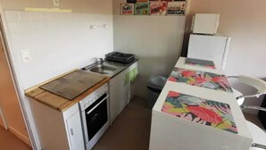A compact kitchen with a sink, stove, and refrigerator. There are colorful posters on the wall and a trash bin. - Homerez - Studio in Gérardmer (Gérardmer)