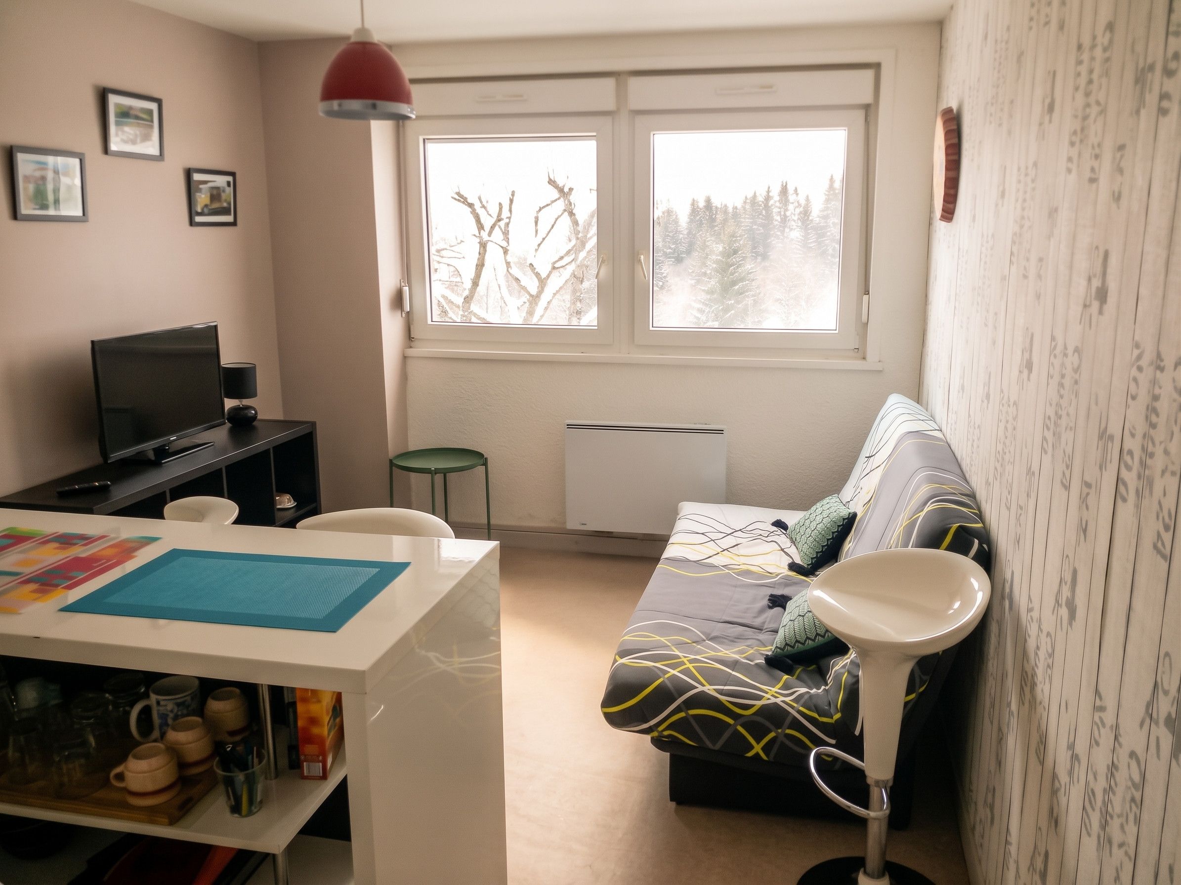 Una sala de estar moderna con un sofá, un televisor, una mesa con tazas y una ventana con vistas a árboles.