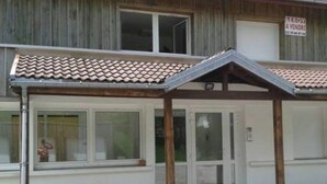 A building with a tiled roof, a covered entrance area, and a sign indicating it is for sale. - Homerez - Studio in Gérardmer (Gérardmer)