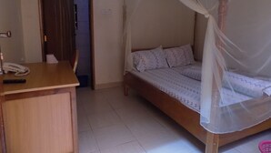 Een slaapkamer met een bed onder een baldakijn, een bureau met telefoon, en een deur naar een andere kamer.