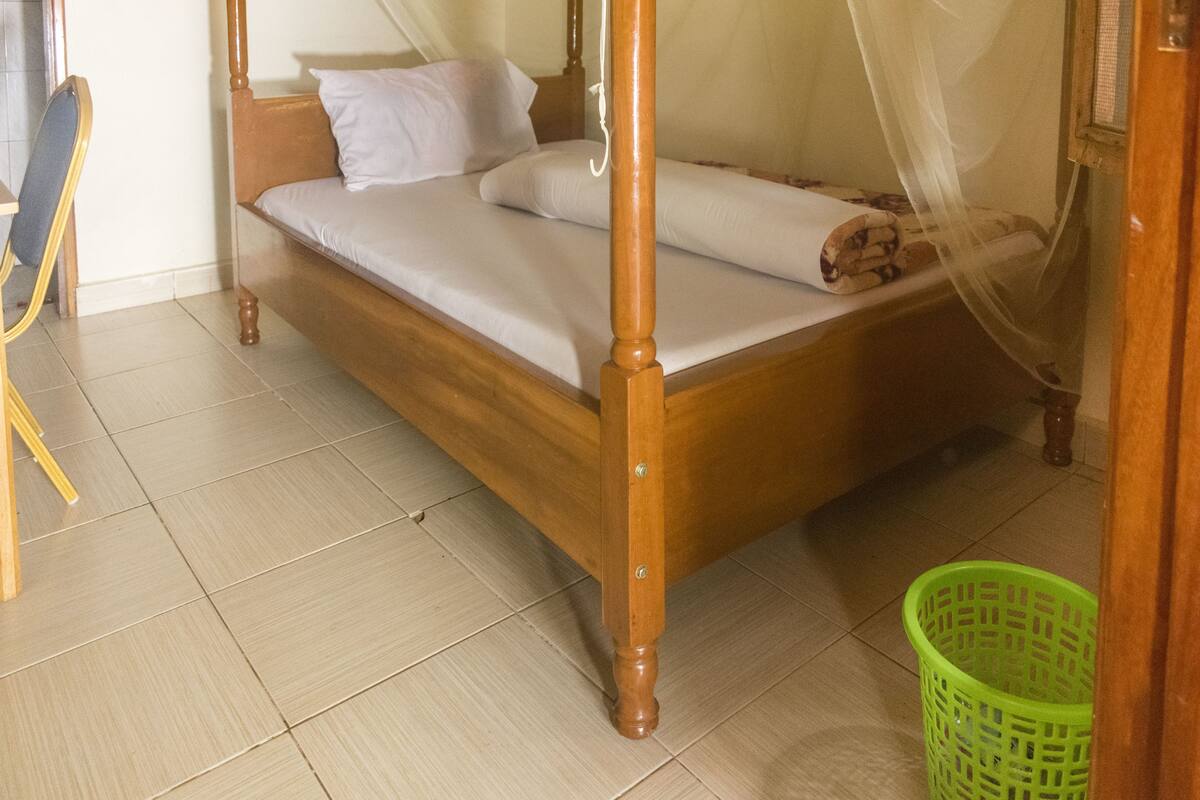 Un lit à baldaquin, un panier à linge vert et une chaise en bois.