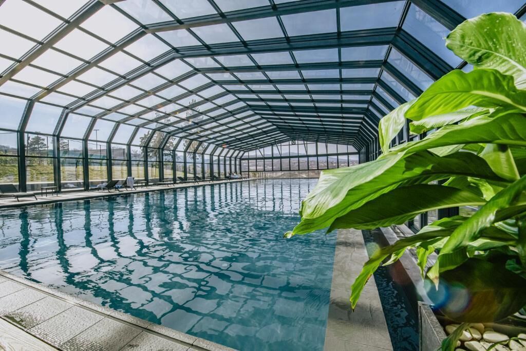 A swimming pool with a glass ceiling structure, surrounded by greenery.
