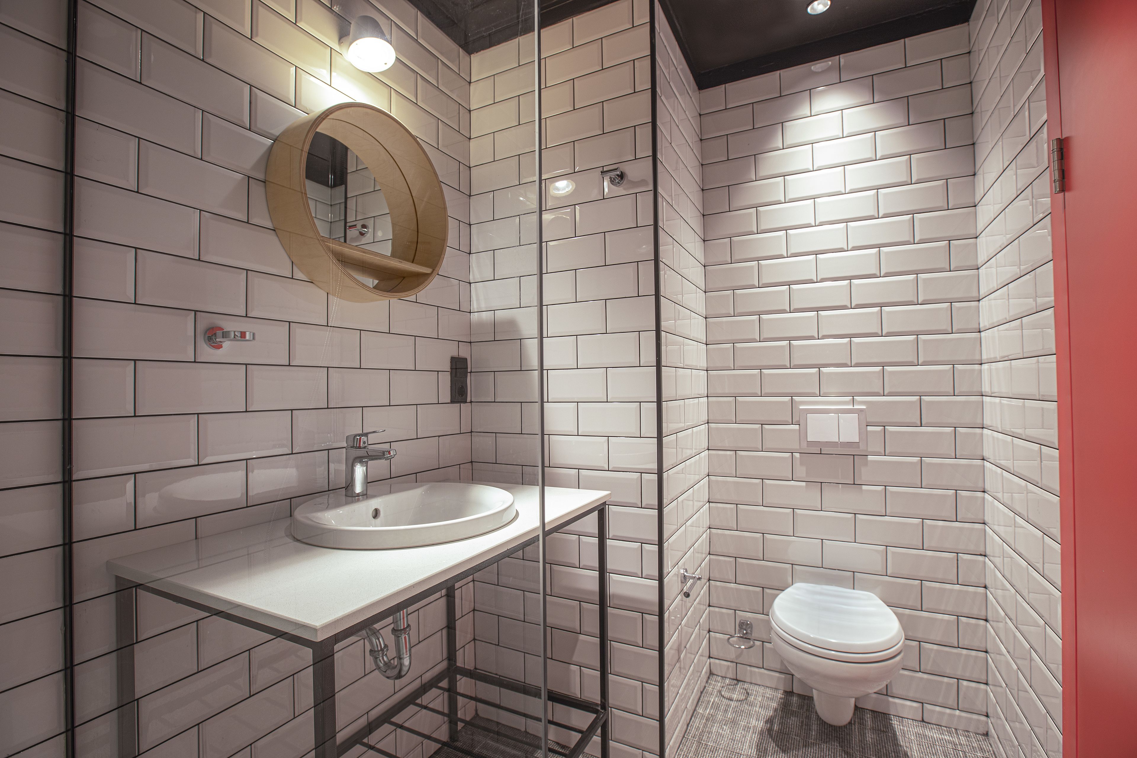 Une salle de bain moderne avec un lavabo blanc, un miroir rond et des toilettes.