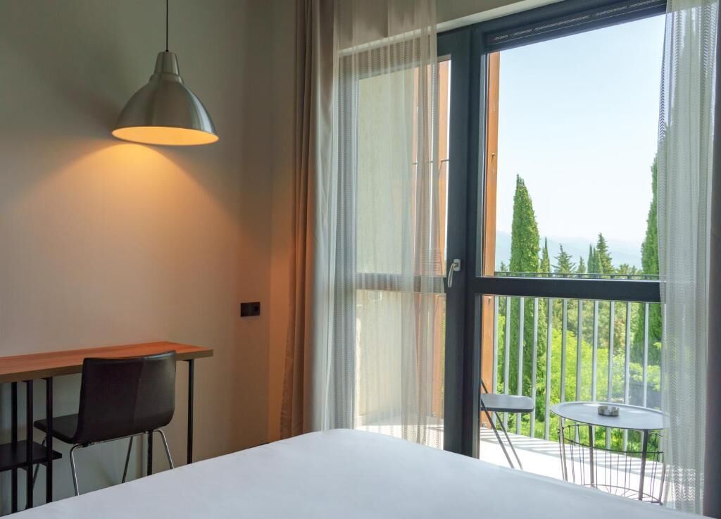 A hotel room with a bed, a desk, a chair, and a balcony with a view.
