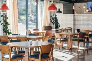 L’intérieur d’un restaurant moderne, avec des tables et des chaises en bois, un éclairage suspendu et une vue sur la rue.