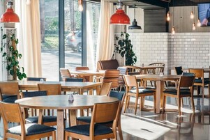 Interior moderno de restaurante con mesas y sillas de madera, iluminación colgante y vistas a la calle.
