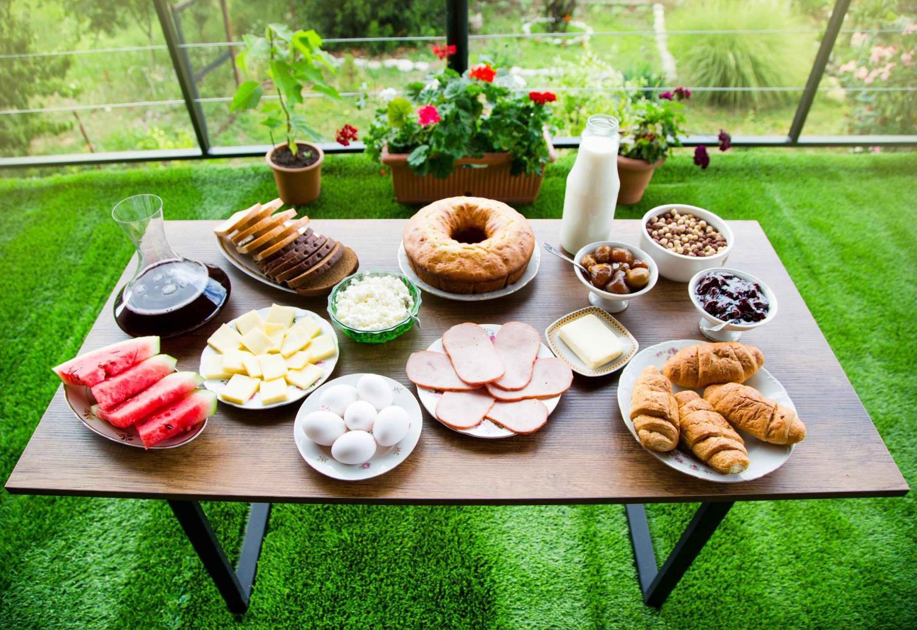 Une table de pique-nique, dressée de divers plats et boissons, entourée d’un jardin luxuriant et verdoyant.