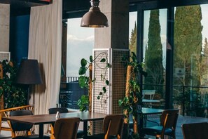 A dining area with tables and chairs, large windows, and indoor plants. - Park Hotel Tsinandali Estate (Telavi)