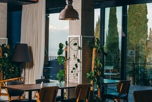 Un comedor con mesas y sillas, ventanas amplias y plantas de interior.