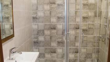 Un baño con ducha de cristal, lavamanos y espejo.