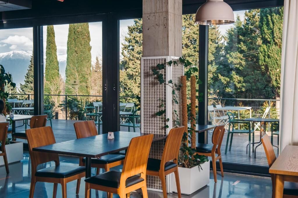 An indoor dining area with tables and chairs, large windows, and a view of trees and mountains.