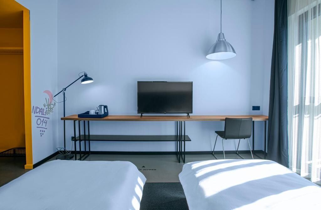 Una habitación de hotel con una cama, un escritorio con televisor, una silla y una lámpara.
