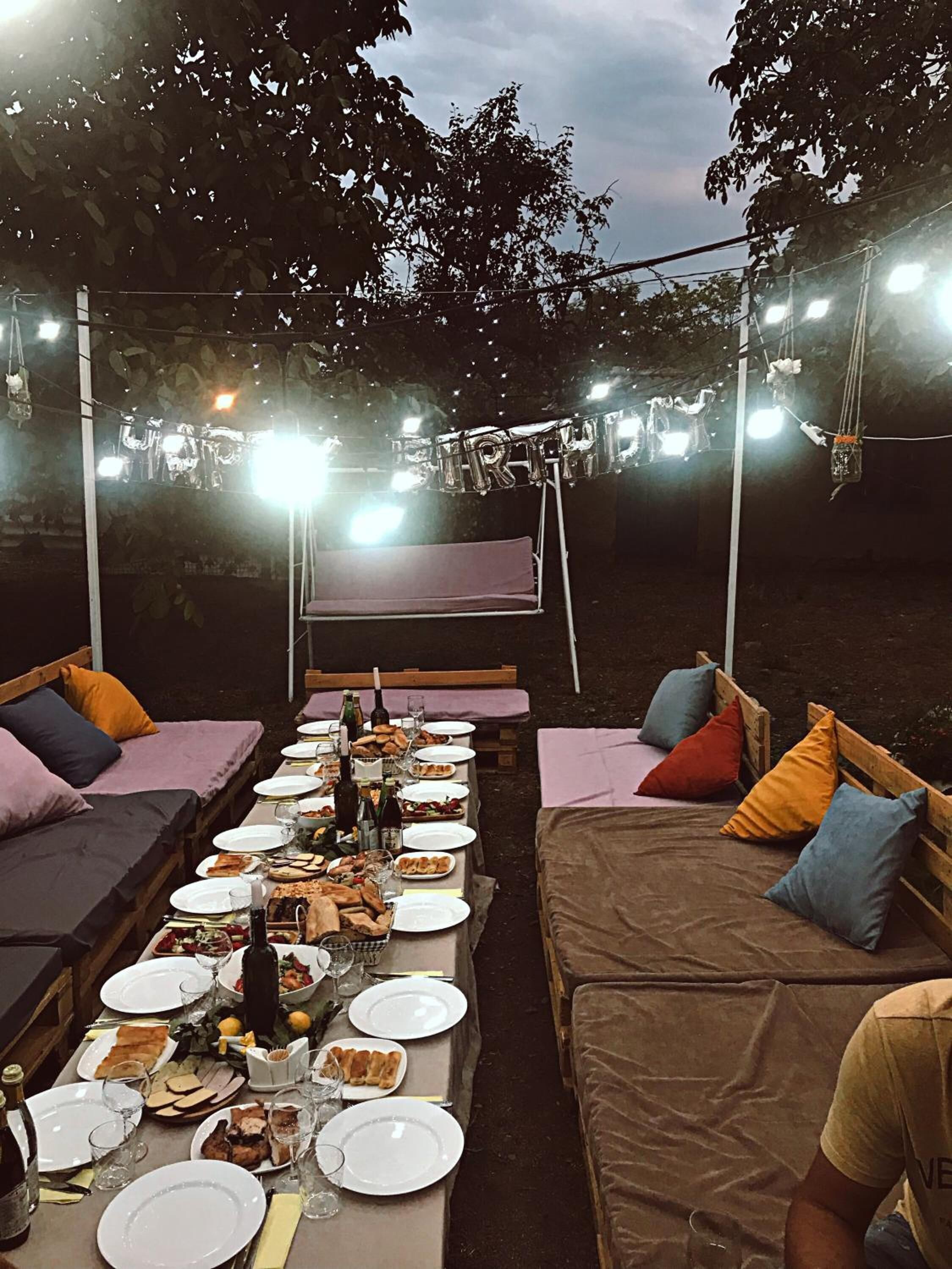 An outdoor dining area with tables set for a meal, surrounded by wooden benches with cushions.