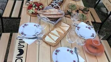 An outdoor wooden table set for a meal with plates, cutlery, glasses, and a variety of food items.
