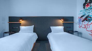Ein Hotelzimmer mit zwei Einzelbetten, einem dunklen Kopfteil, Nachttischlampen, einem kleinen Tisch und einer Wand mit einem farbenfrohen Wandgemälde.