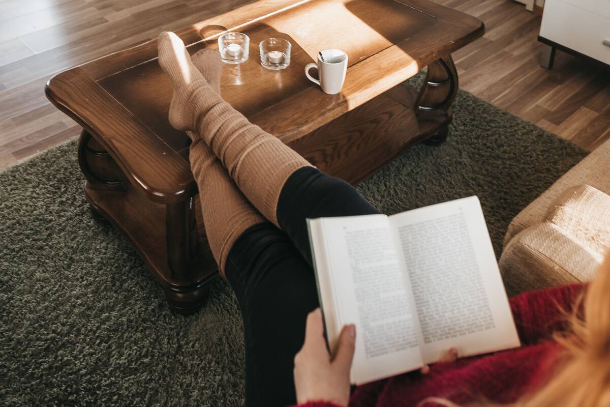 A cozy living room with a fireplace, a coffee table, and a person reading a book.