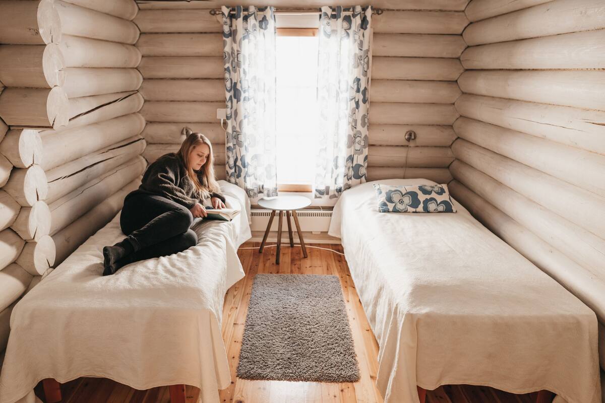 A log cabin room with two beds, a small table, and a window with curtains.