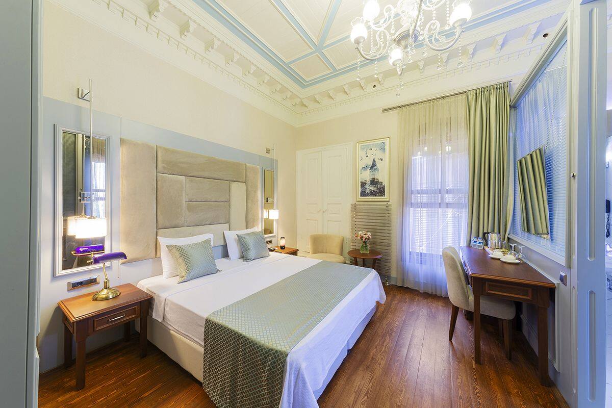 Habitación de hotel con una cama grande, un escritorio, una silla, una lámpara de escritorio, un espejo y una araña.