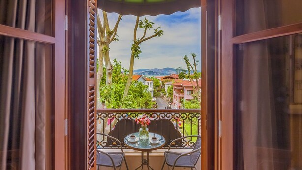 A balcony with a table and chairs, a view of a street and buildings, and a tiled floor. - No 2 Hotel By Şükrü (Adalar)