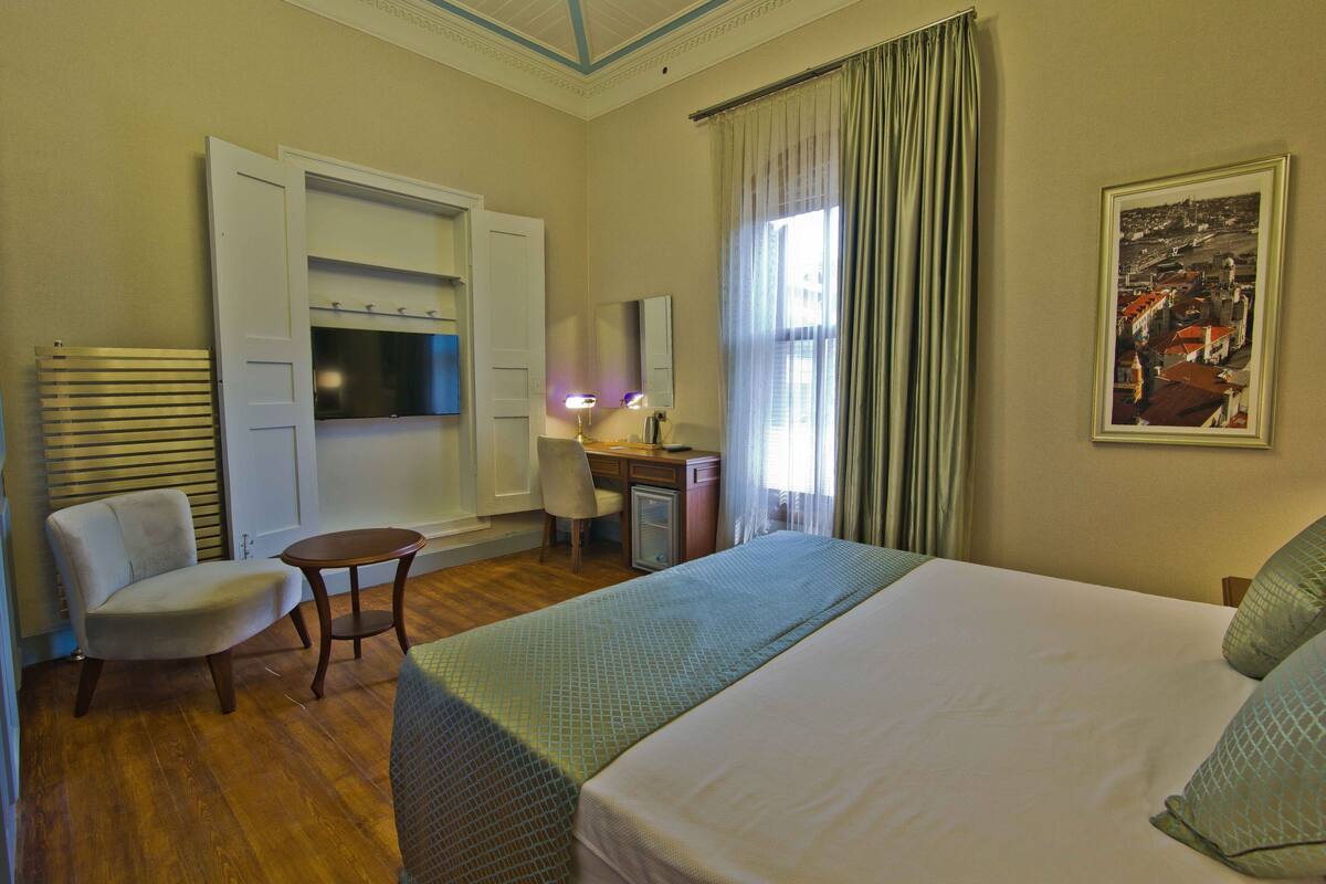 Habitación de hotel con cama, escritorio, silla, lámpara y un cuadro en la pared.
