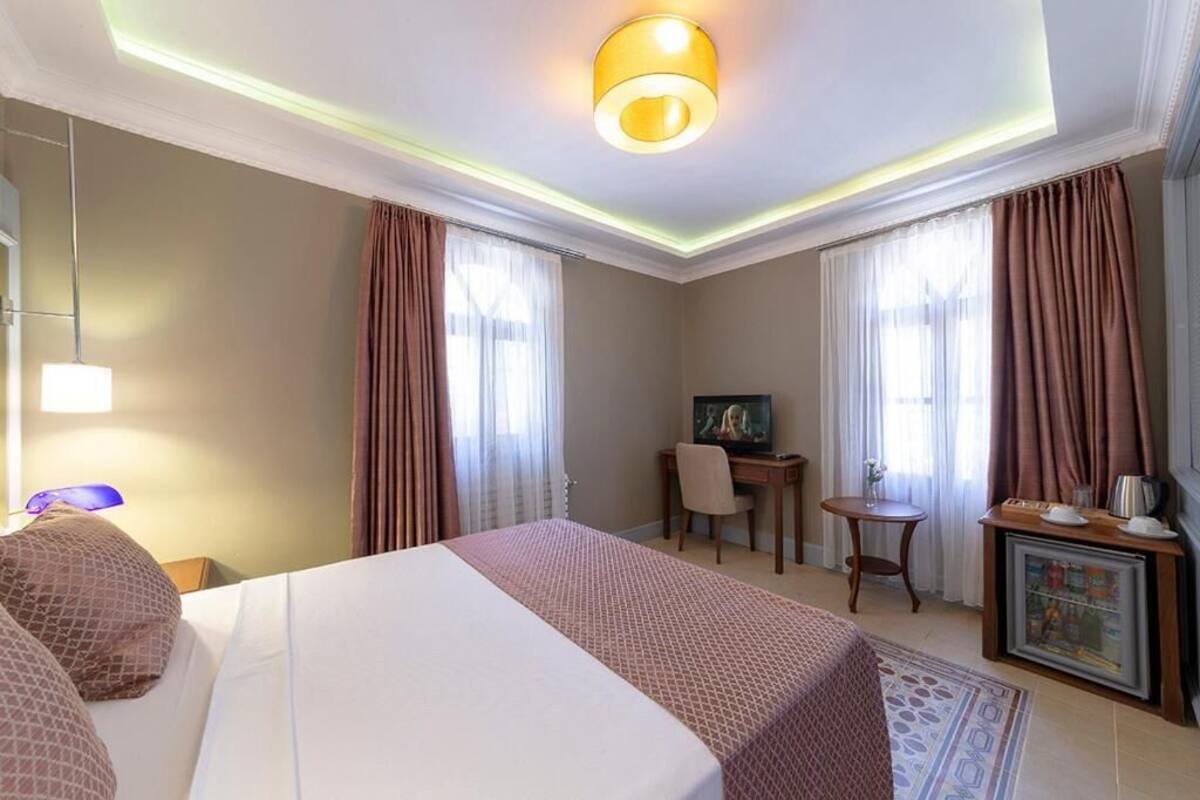 Habitación de hotel con una cama grande, un escritorio con silla, un televisor y una mesita de noche con lámpara.
