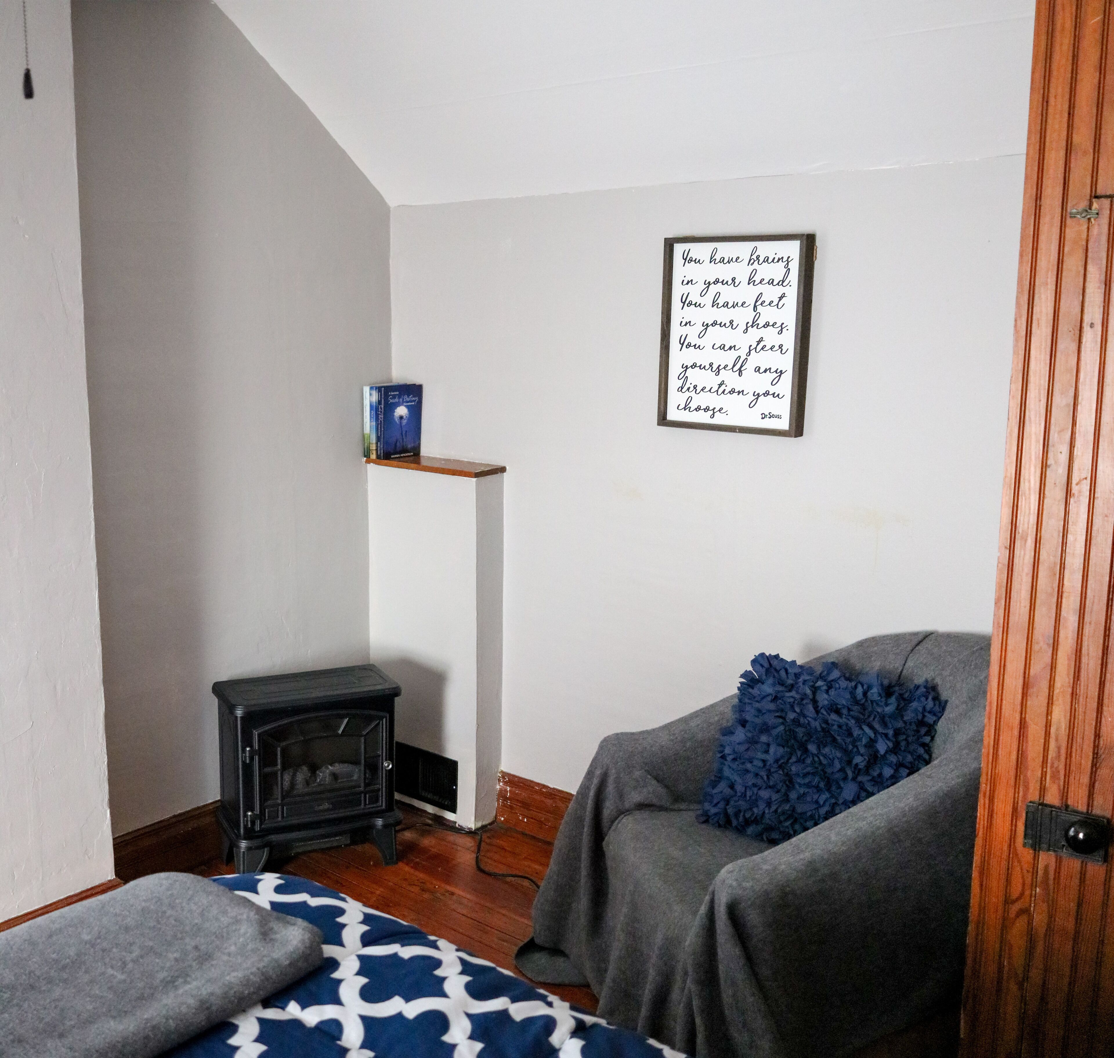 A cozy room with a fireplace, a comfortable chair, a small shelf with a book, and a motivational quote on the wall.