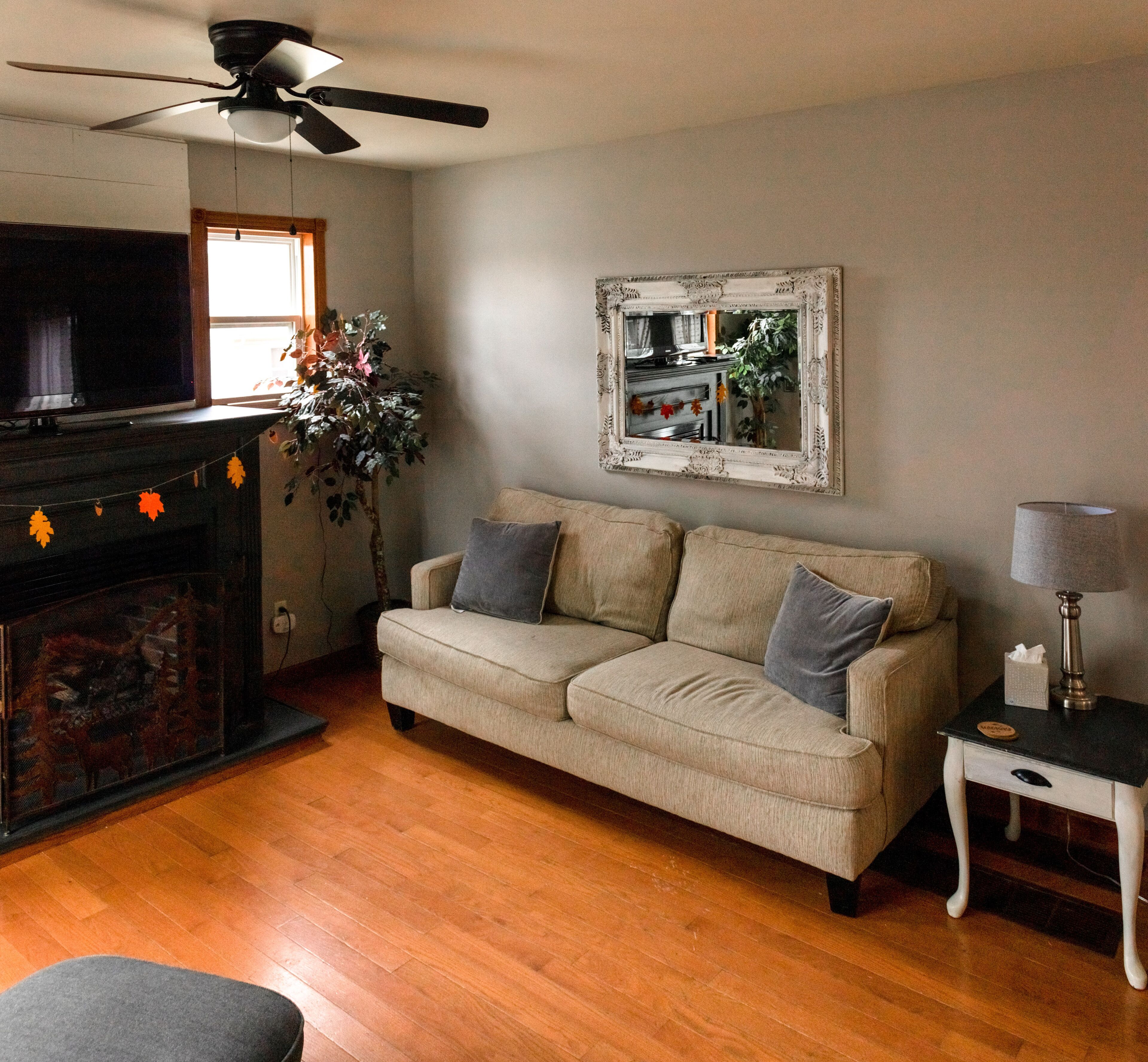 A living room with a beige sofa, a television, a fireplace, and a ceiling fan.