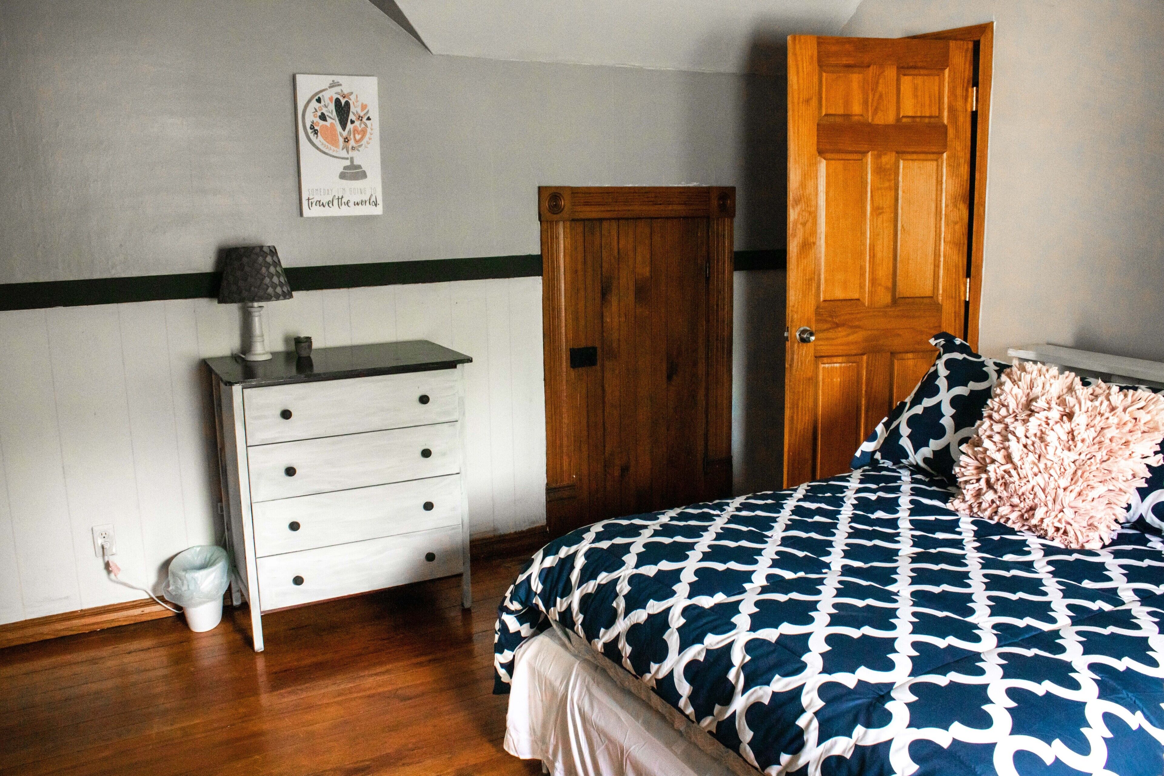 A bedroom with a wooden door, a white dresser, and a bed with a patterned bedspread.