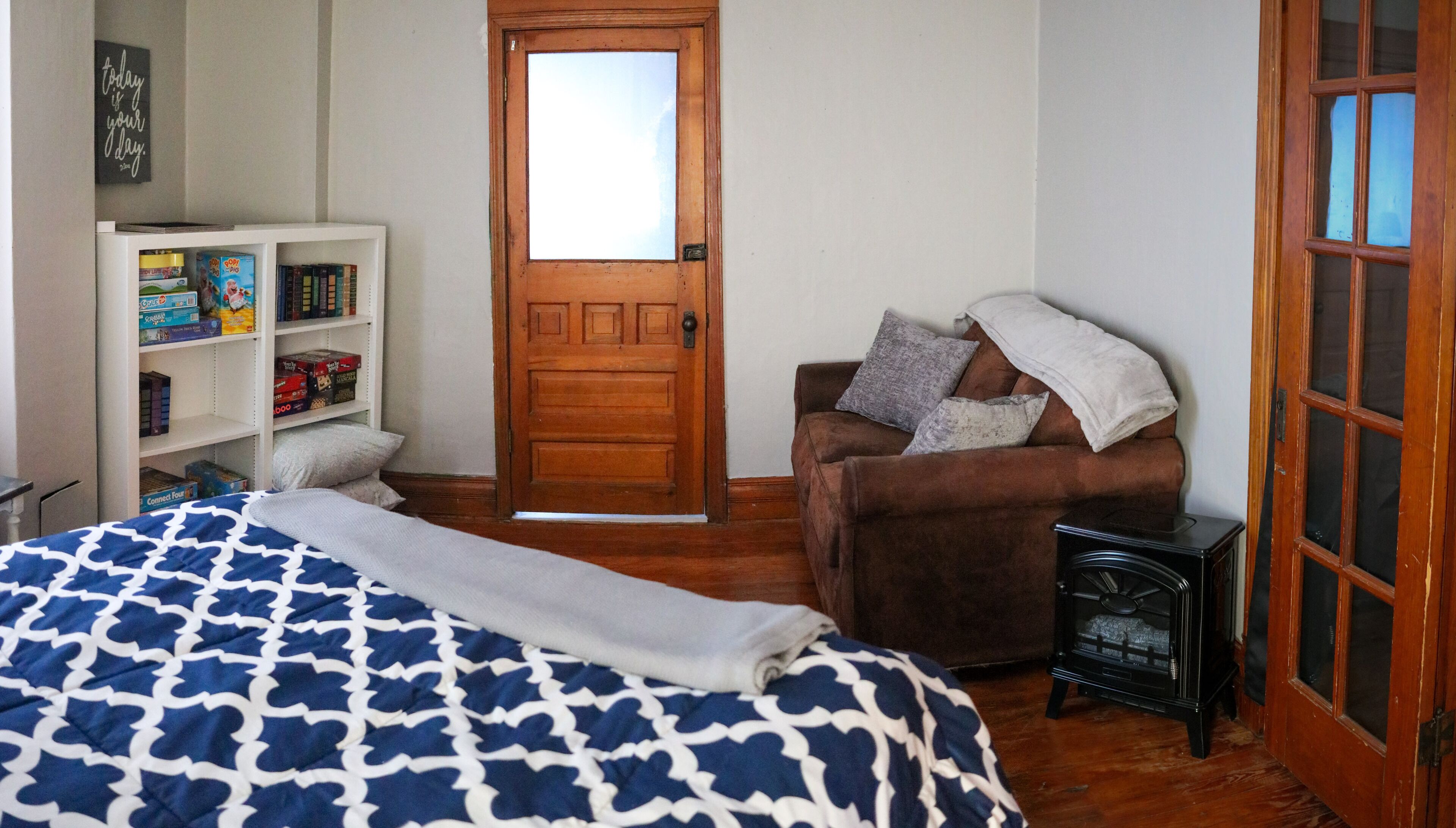 Een slaapkamer met een bed, een bruine fauteuil, een boekenkast en een houten deur.