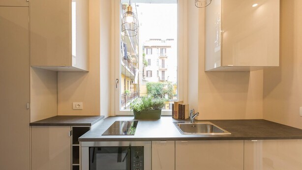 Una cocina moderna con horno empotrado, microondas y lavamanos. Se ve una ventana con vistas a edificios.