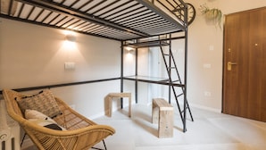 Una habitación con techo alto, una silla de ratán, un banco de madera, una escalera y una puerta.