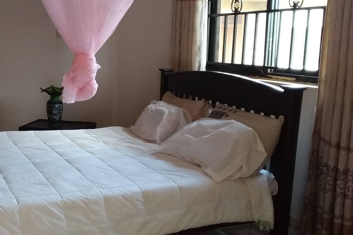 Une chambre à coucher avec un lit, une table de chevet, une chaise et une fenêtre avec des rideaux.