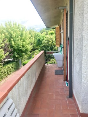A balcony with a tiled floor, a white bench, a red broom, and a green garden hose.