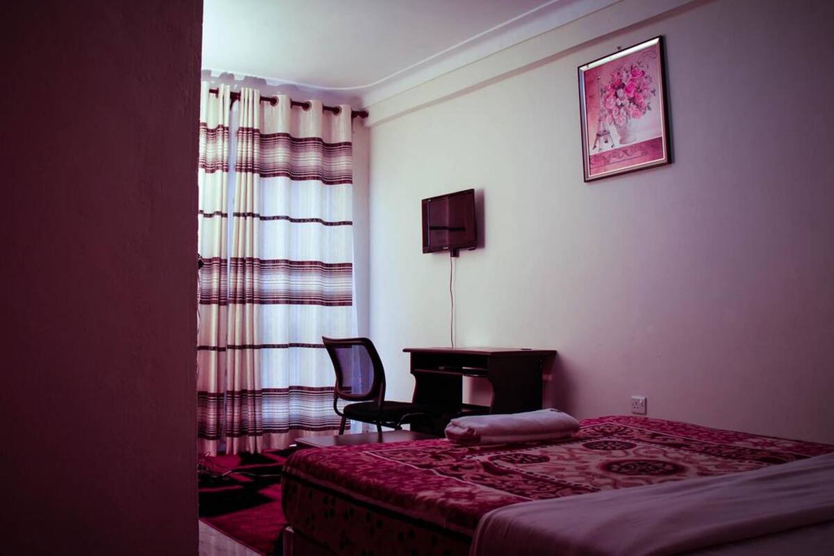 A hotel room with a bed, a desk, a chair, a TV, and a window with curtains.