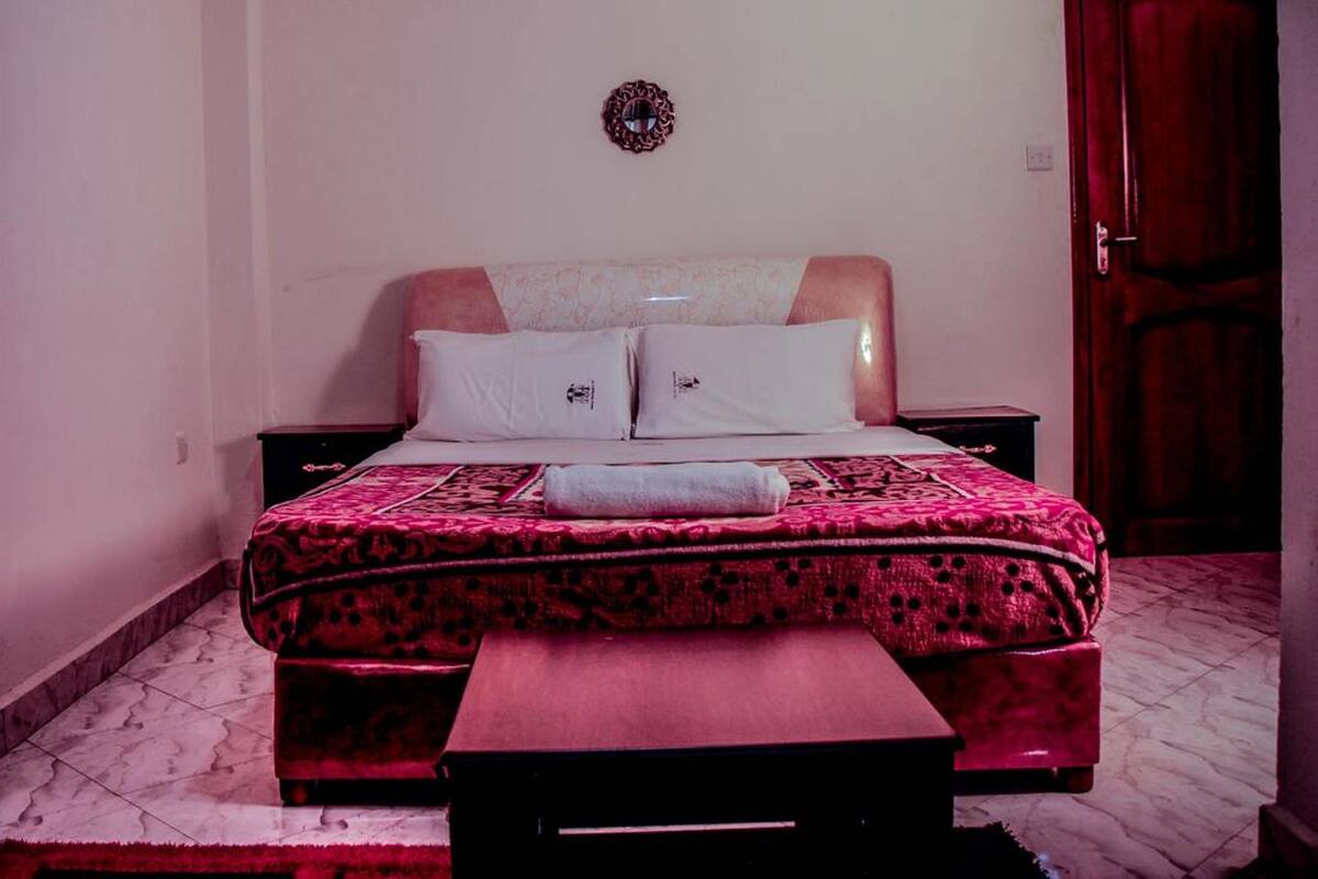 A bed with a patterned bedspread and pillows, a bedside table, and a wooden bench.