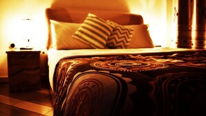 A bed with patterned bedding, a nightstand with a lamp, and a wall with a column. - Mbale Travellers Inn (Mbale)