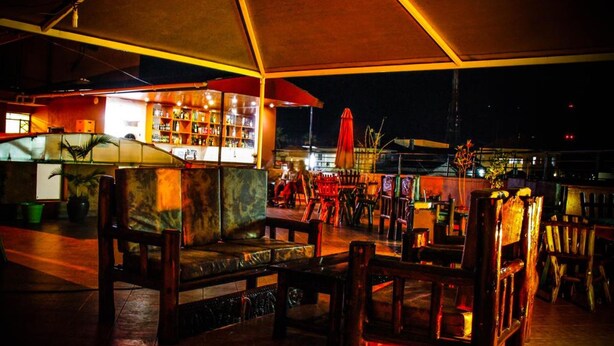 An outdoor seating area with wooden furniture and a bar in the background. - Mbale Travellers Inn (Mbale)