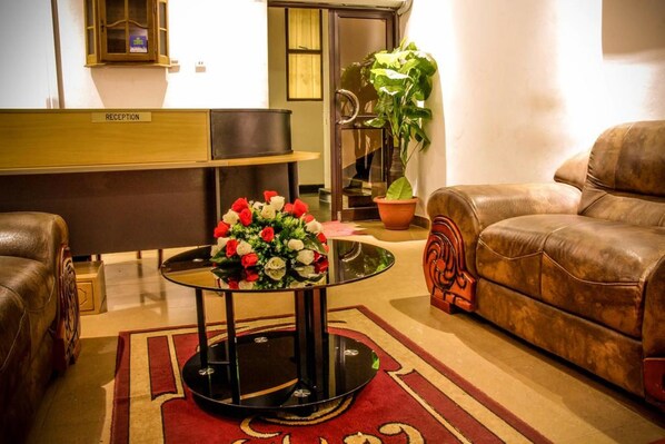 Una zona de recepción con mostrador, una mesa redonda con un florero, un sofá de cuero marrón y una planta en maceta.
