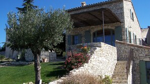 A stone building with a sloped roof, a staircase leading to the entrance, and a tree in the foreground. - Stone barn 360 ° view of the Luberon and the Vaucluse mountains (Viens)