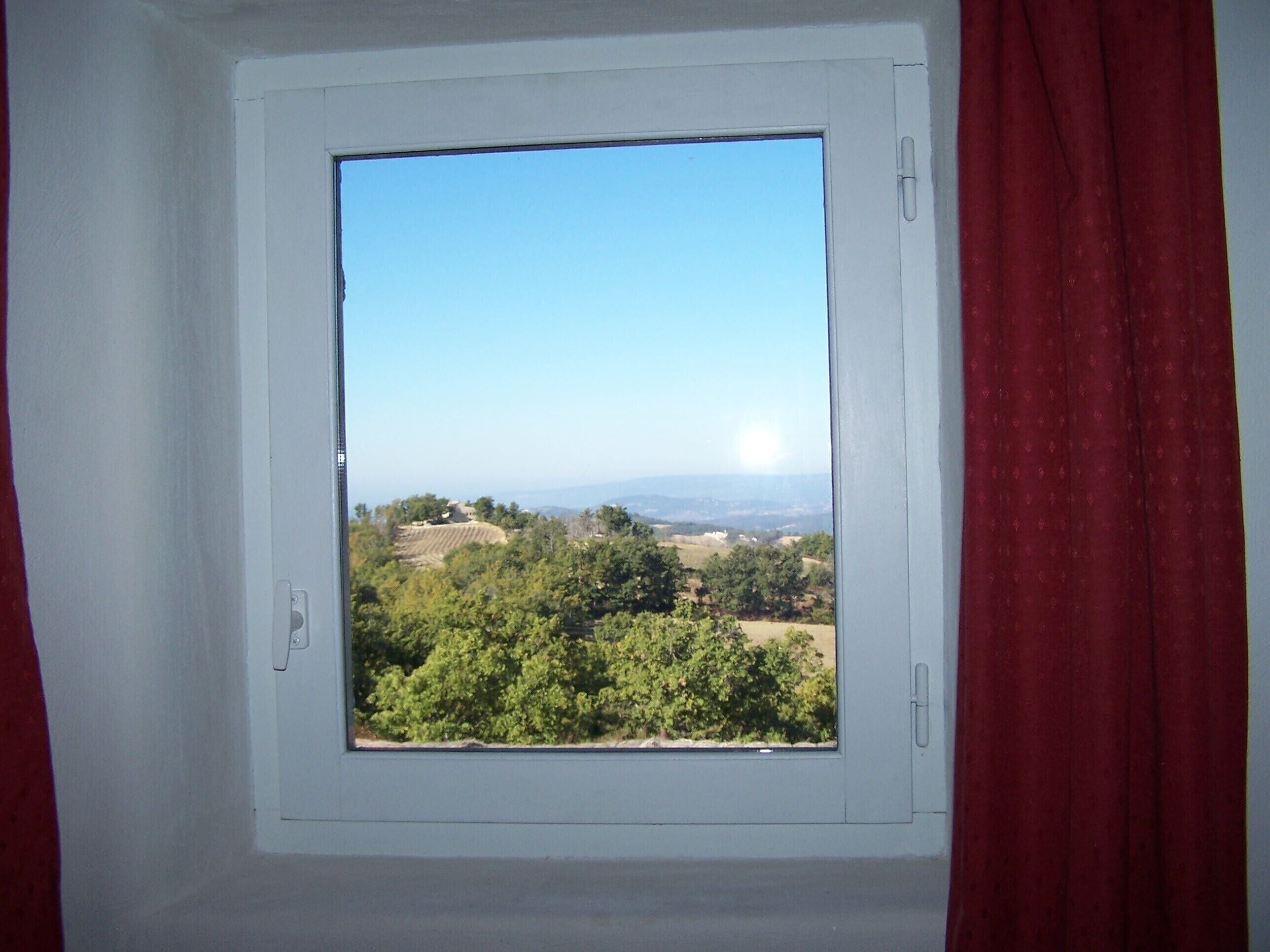 A window with a clear view of a green landscape and distant hills.