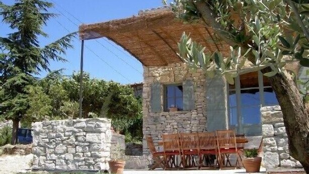 A stone building with a thatched roof, a wooden table and chairs, and a potted plant. - Stone barn 360 ° view of the Luberon and the Vaucluse mountains (Viens)