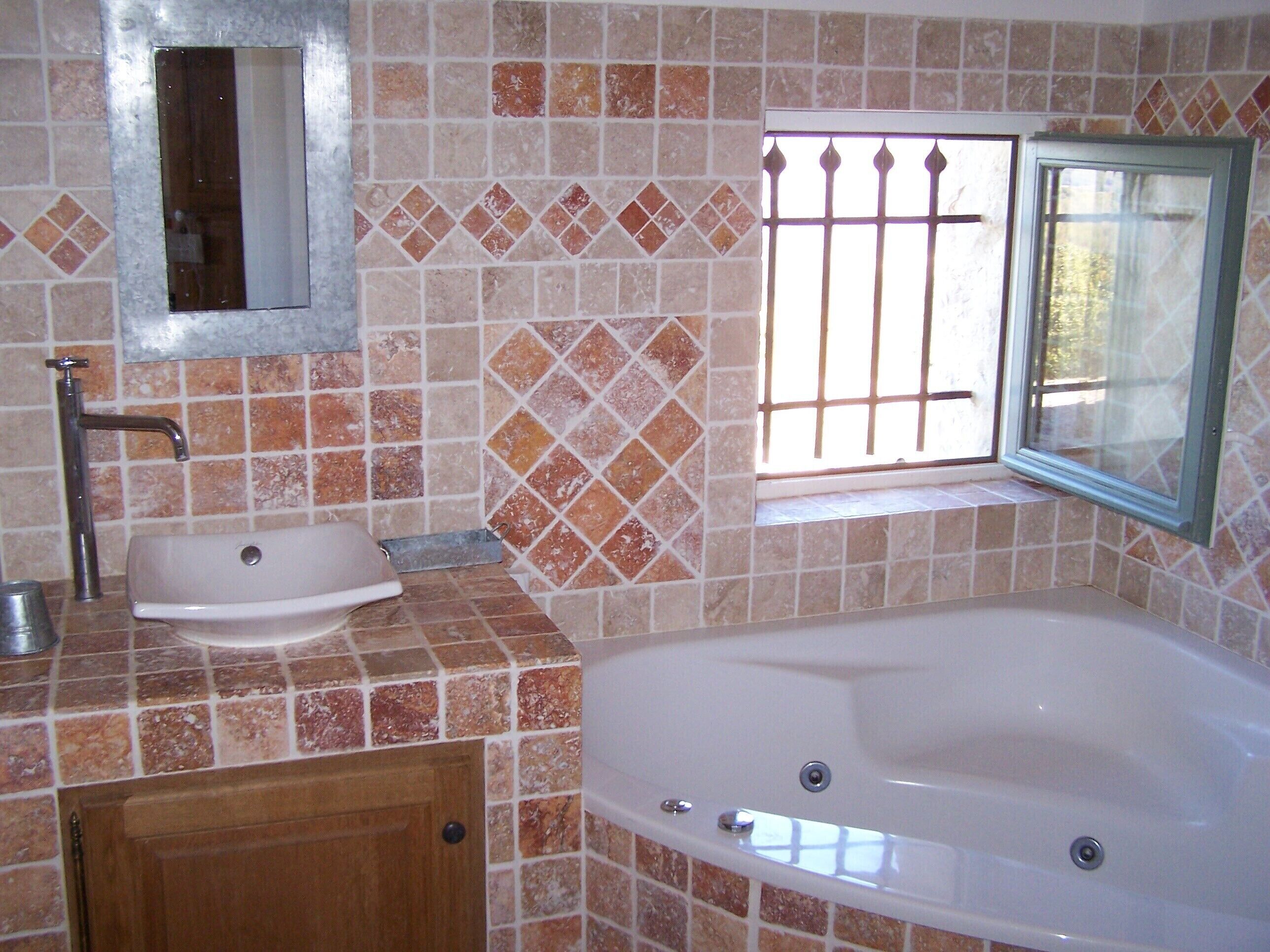 A bathroom with a sink, mirror, window, and bathtub.