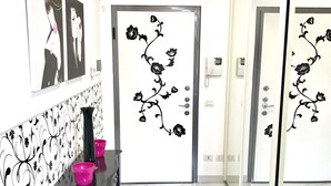 A room with a black and white patterned wall, a black table with pink bowls, a chair, and a door with floral decals. - Sarpi Apartment (Milan)