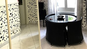 A dining area with a round table and chairs, a chandelier, and a large window with curtains. - Sarpi Apartment (Milan)