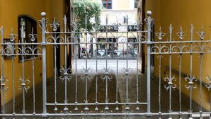 A gated entrance with ornate metalwork, leading to a building with a yellow facade and a visible shop sign. - Sarpi Apartment (Milan)