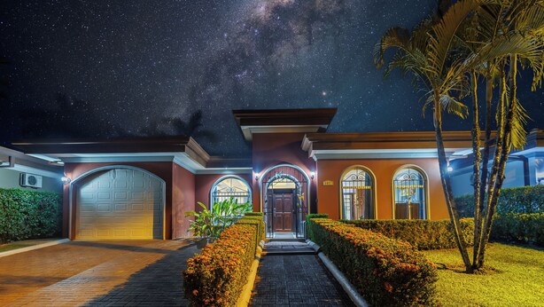 Una casa residencial bien iluminada con garaje, entrada arqueada y un cielo nocturno estrellado.