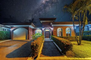 Una casa residencial bien iluminada con garaje, entrada arqueada y un cielo nocturno estrellado.