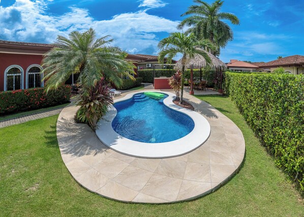 Una piscina de borde curvo, rodeada de un césped cuidado y palmeras.