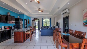 Una cocina amplia con armarios oscuros, una isla central y un comedor con sillas de madera y una mesa de vidrio.