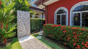 Un jardín bien cuidado con un camino pavimentado, un muro de azulejos y un edificio rojo con ventanas arqueadas.